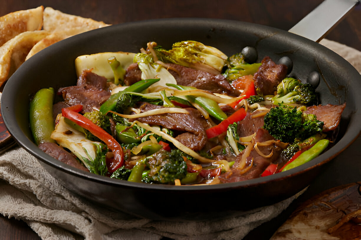 A sizzling stir-fry with beef and colorful vegetables in a black pan, accompanied by crispy dumplings.