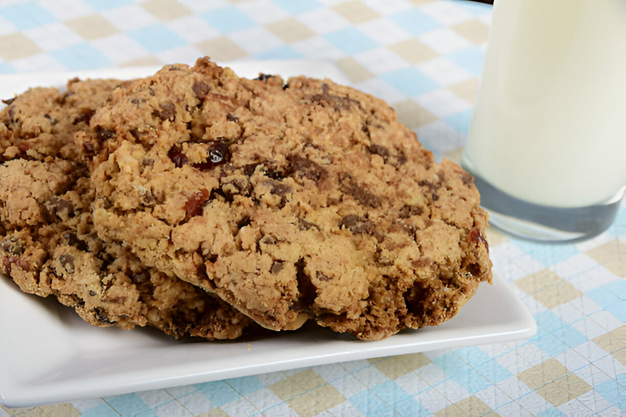 Two large homemade cookies on a white plate next to a glass of milk.