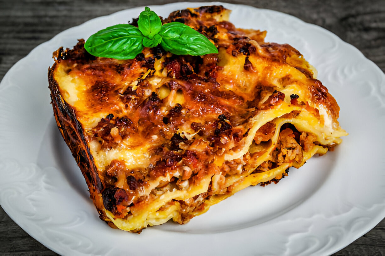 A slice of delicious lasagna topped with a fresh basil leaf on a white plate.