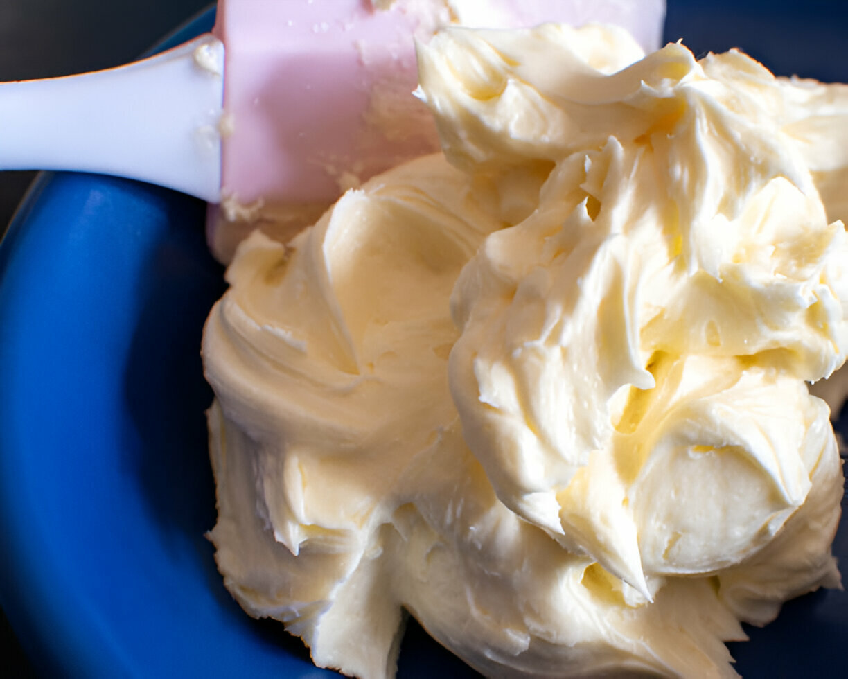 Close-up of creamy butter or frosting in a blue bowl with a pink spatula.