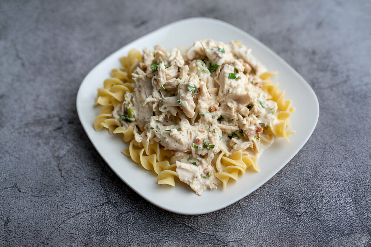 A plate of chicken and pasta with a creamy sauce, garnished with green herbs.