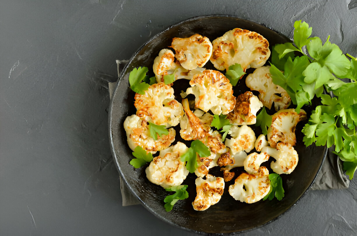 A black bowl filled with roasted cauliflower florets garnished with fresh parsley on a gray surface.