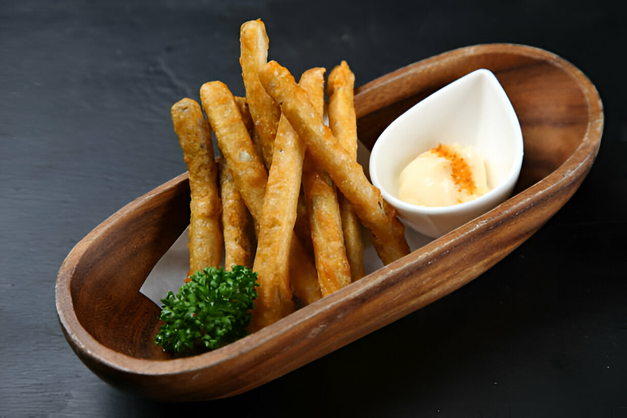 A wooden bowl containing golden-brown fried sticks and a small white dish of creamy dip, garnished with parsley.