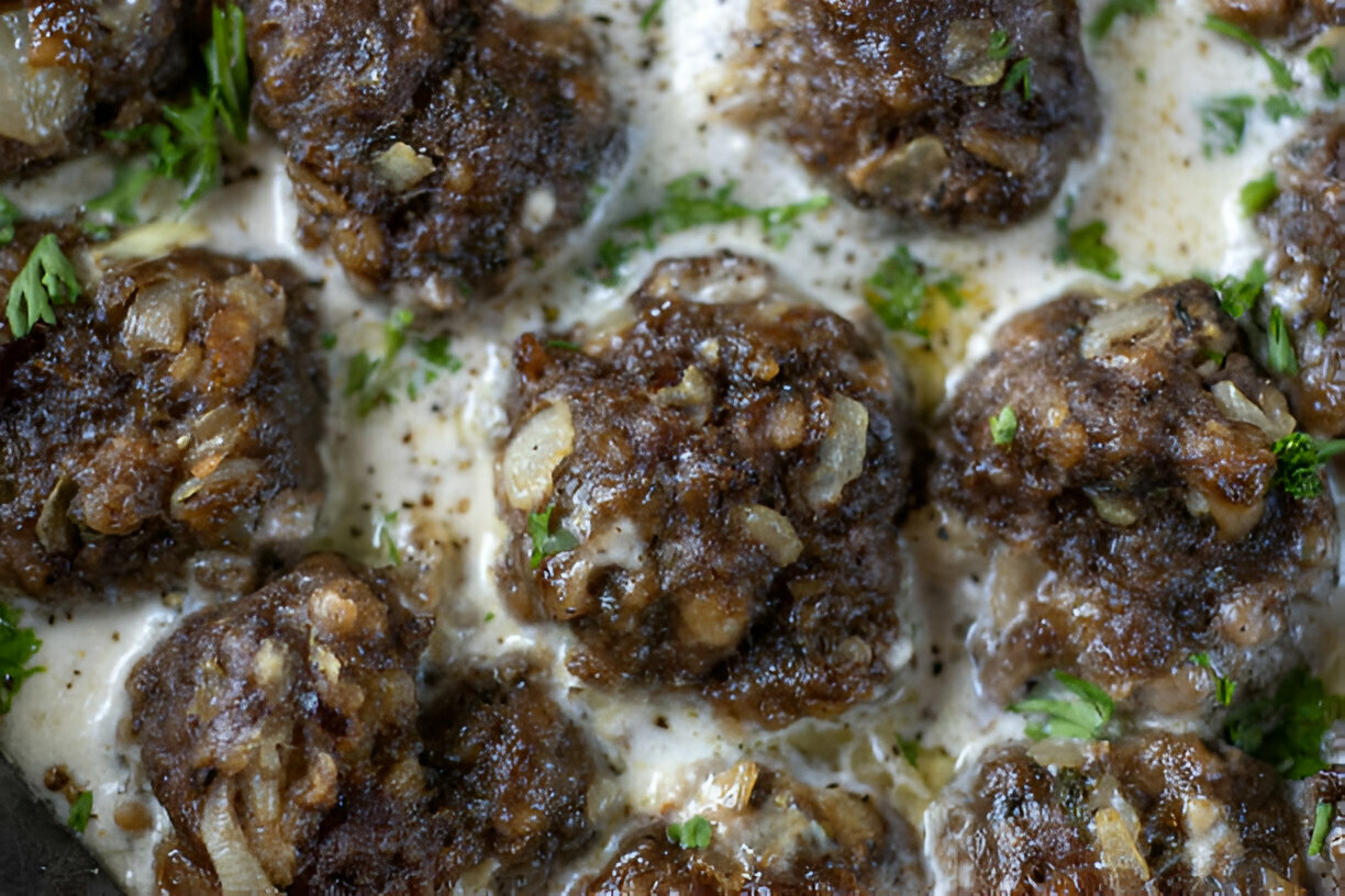 A close-up view of meatballs cooked in a creamy sauce, garnished with fresh herbs.