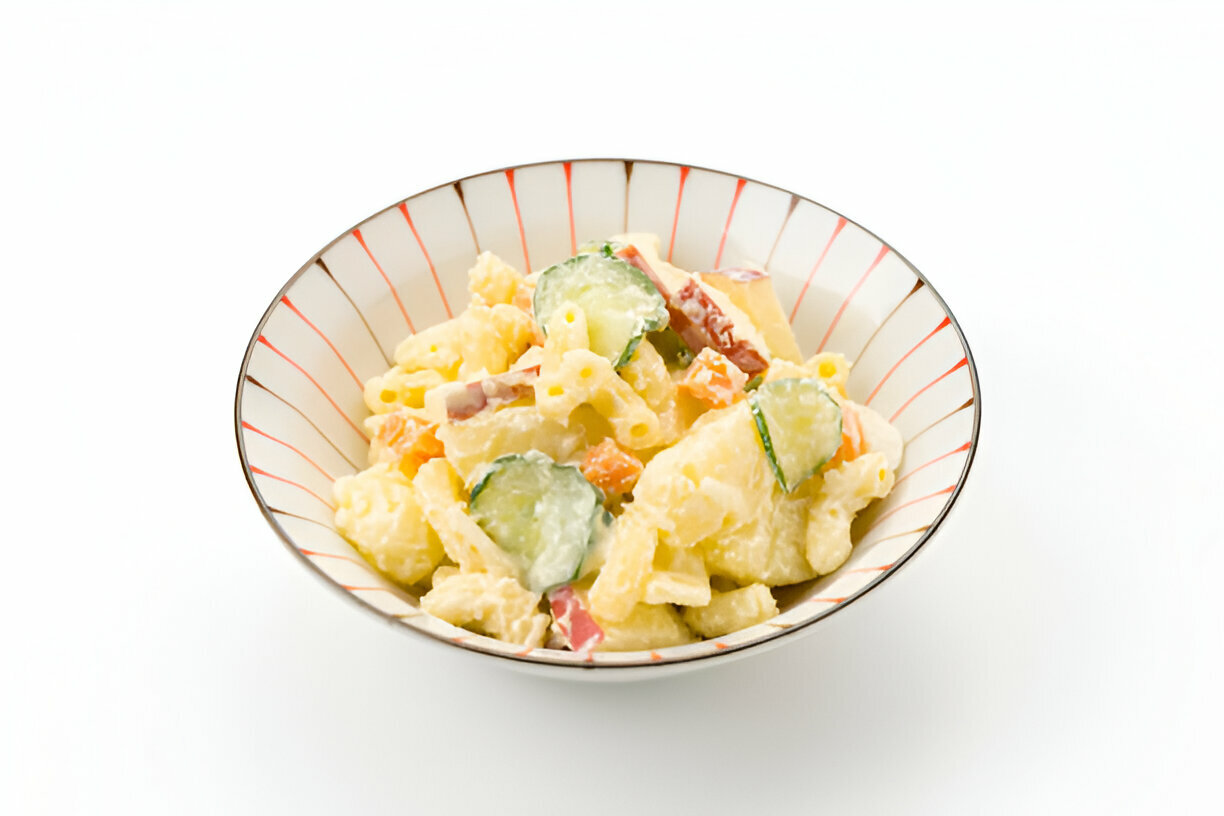 A bowl of pasta salad with cucumbers and mixed vegetables, served in a decorative dish.