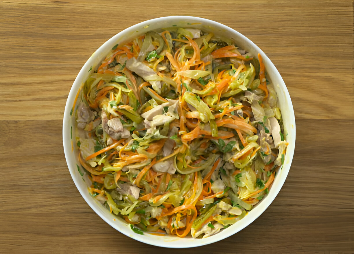 A colorful salad made with shredded vegetables and pieces of chicken in a white bowl on a wooden surface.