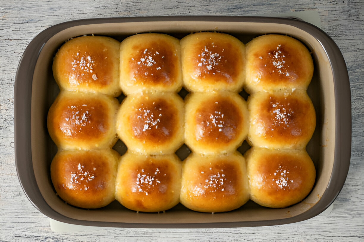 A tray of freshly baked golden dinner rolls sprinkled with sea salt.