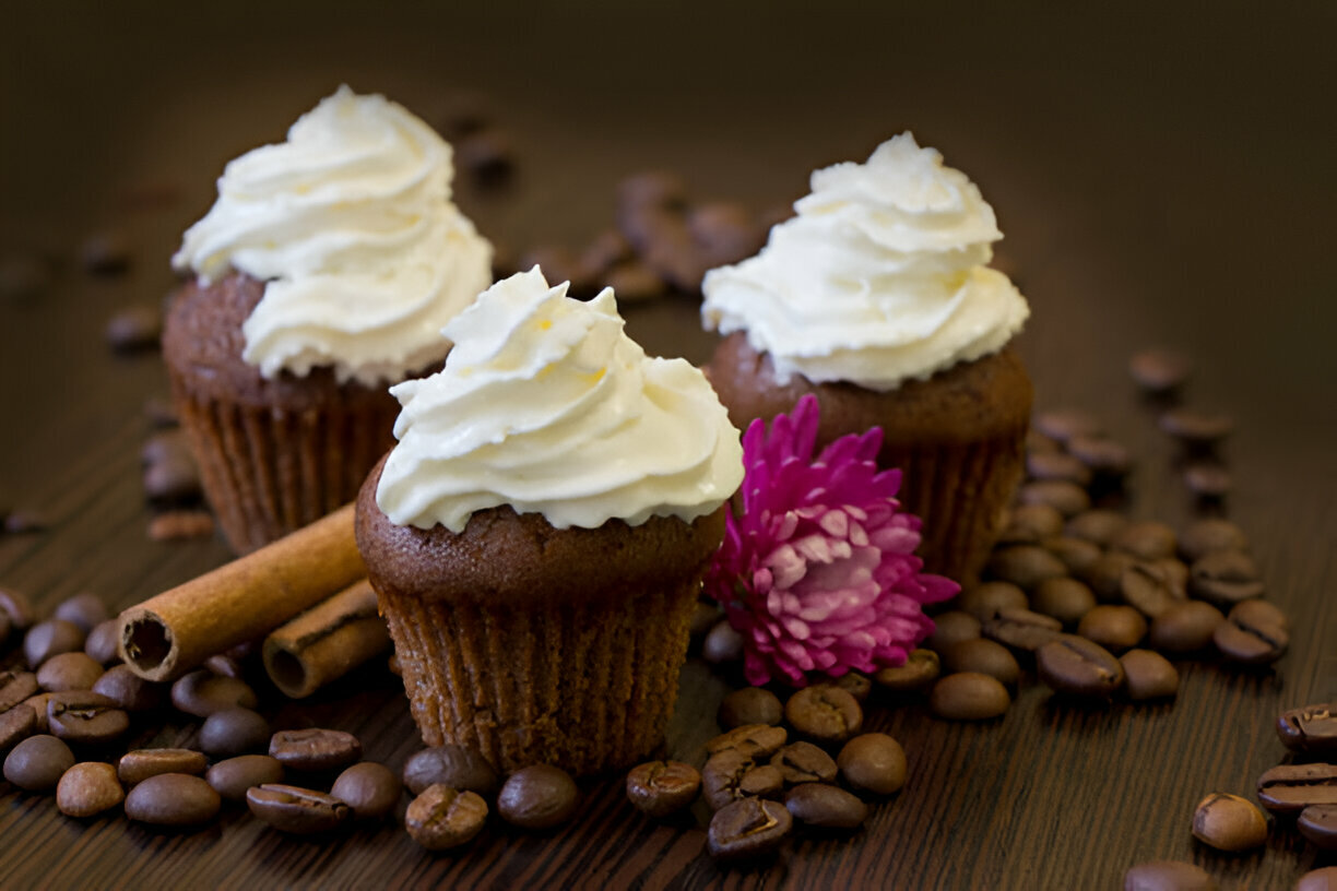 Delicious chocolate cupcakes with white frosting surrounded by coffee beans and a pink flower