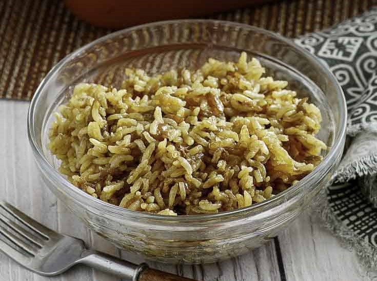 A dish of cooked rice in a glass bowl on a wooden surface.