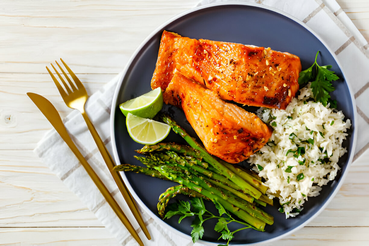 A plate of grilled salmon with lime, asparagus, and rice on a wooden table