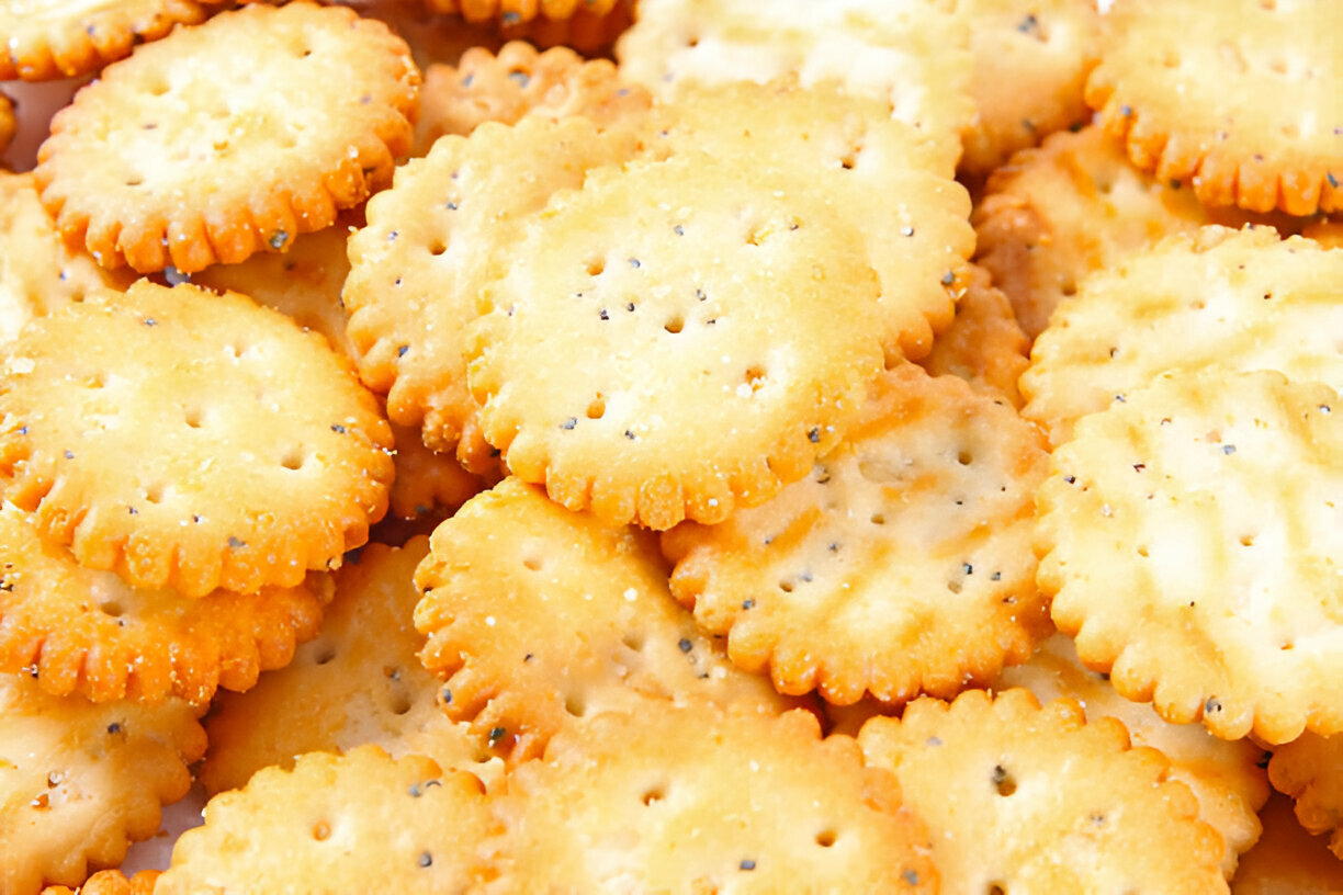 A close-up view of a pile of round, baked crackers with a golden-brown color and scalloped edges.