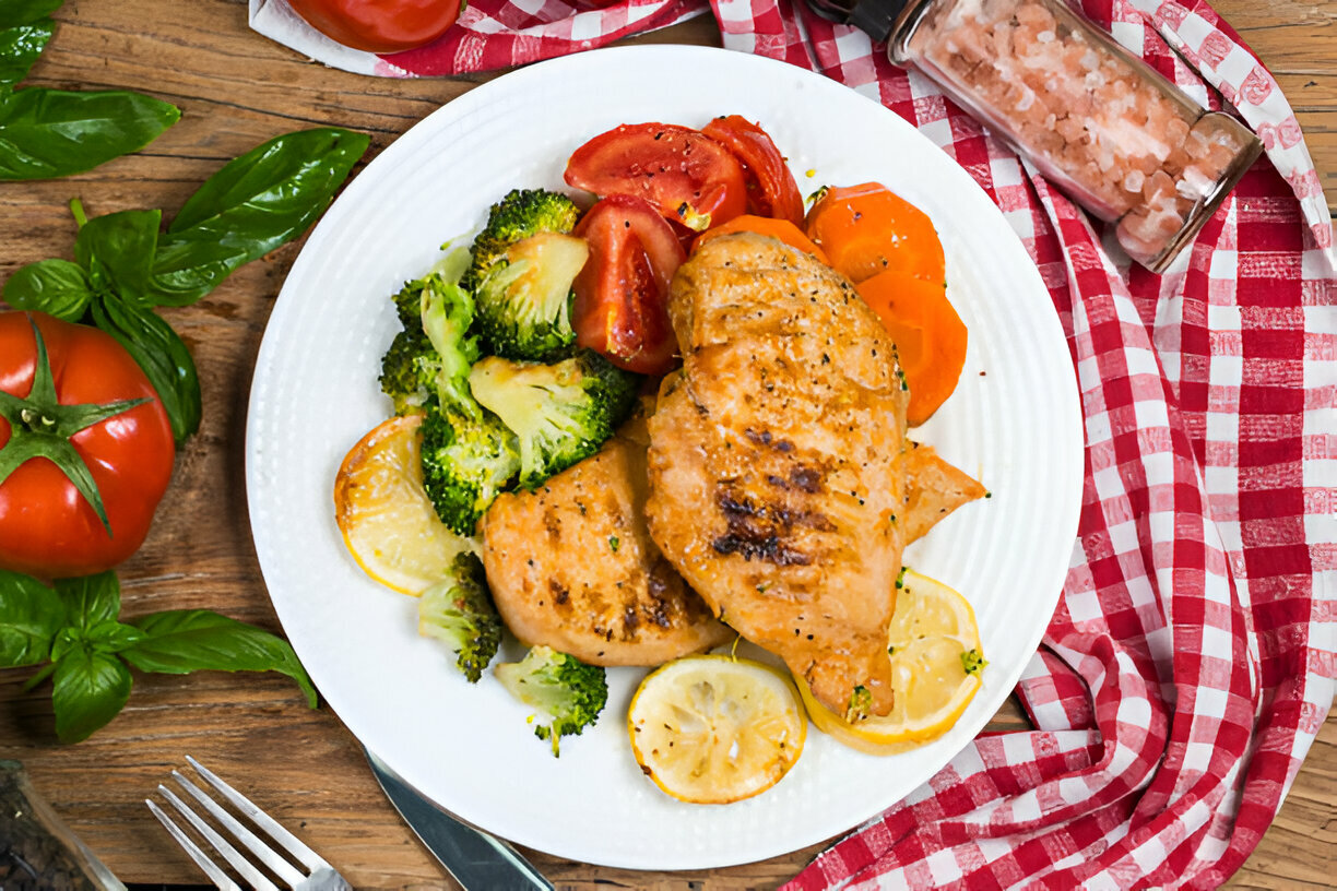 Grilled chicken breast served with broccoli, tomatoes, and carrots on a white plate.