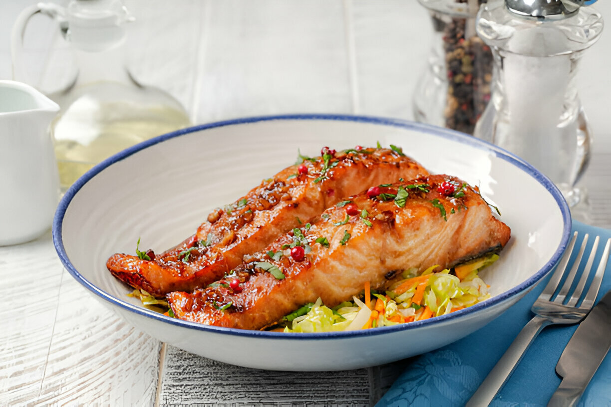 A delicious plate of glazed salmon served on a bed of fresh salad and garnished with herbs.