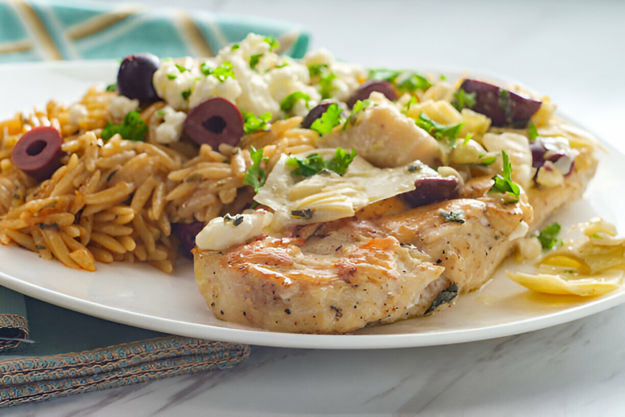 A plate featuring grilled chicken breast with olives and artichokes, served alongside orzo pasta.