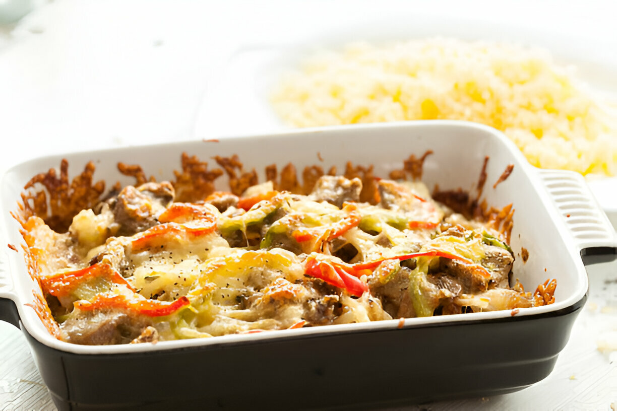 A delicious baked dish with melted cheese, bell peppers, and meat served in a rectangular dish, with a side of fluffy rice.