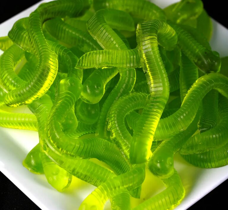 A close-up of green gummy worms piled on a white plate.