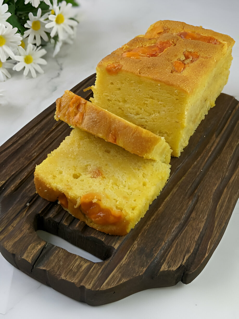 Sliced yellow cake on a wooden board with flowers in the background