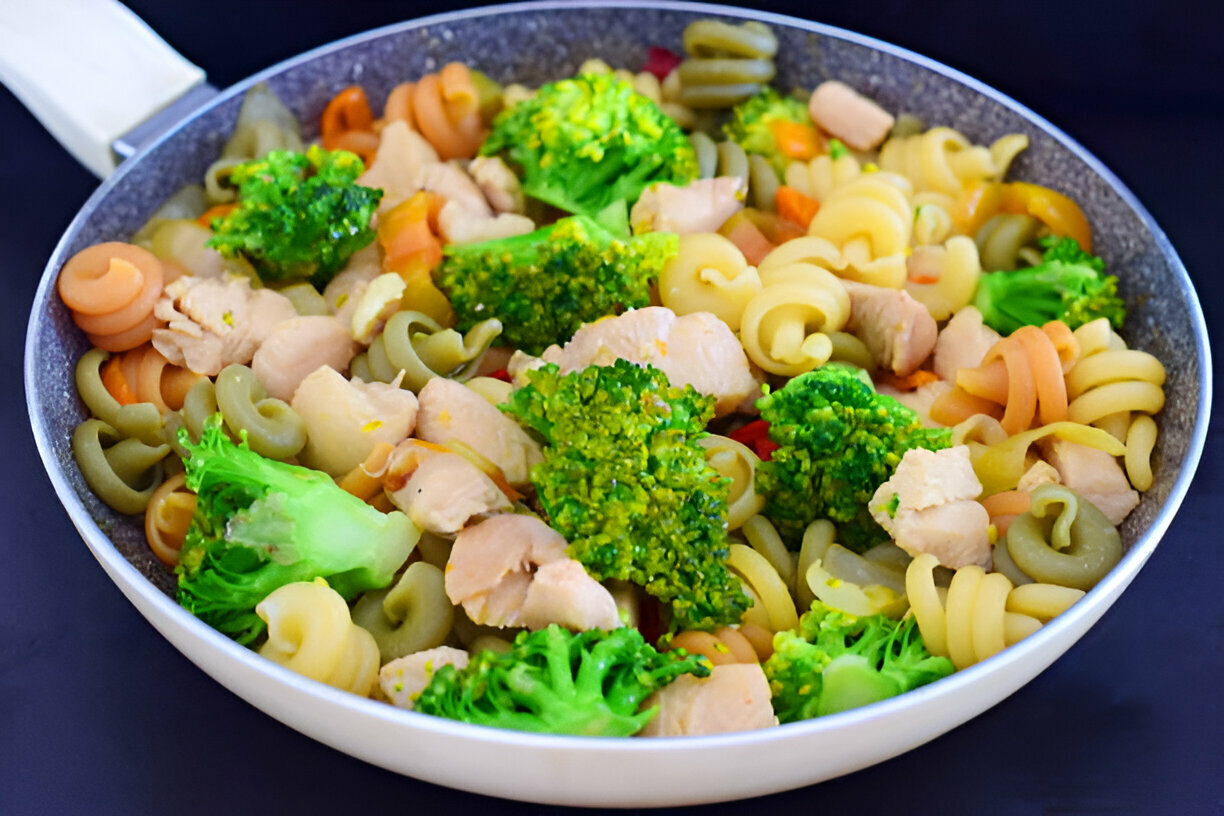 A vibrant dish featuring pasta, broccoli, and pieces of chicken in a pan.