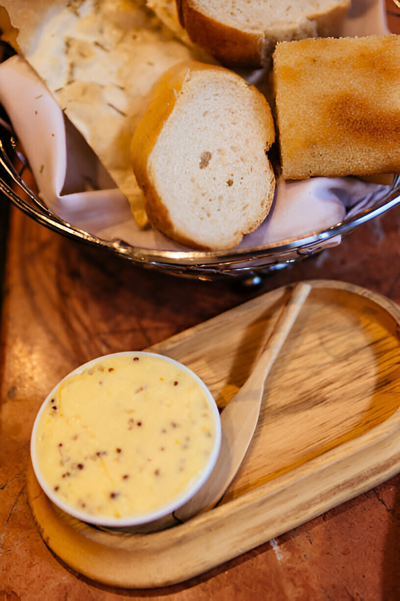 A basket of assorted breads with a bowl of butter on a wooden tray.