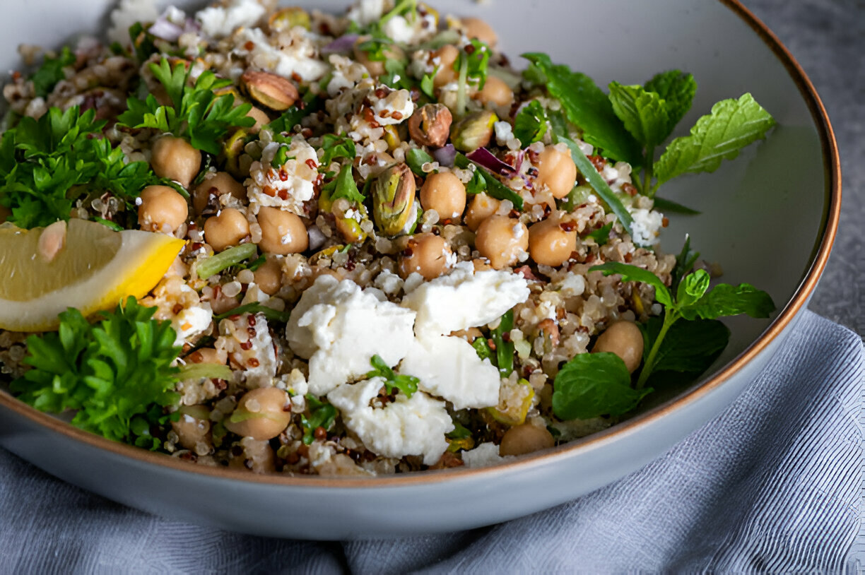 A colorful quinoa salad with chickpeas, herbs, and feta cheese, garnished with a lemon wedge.