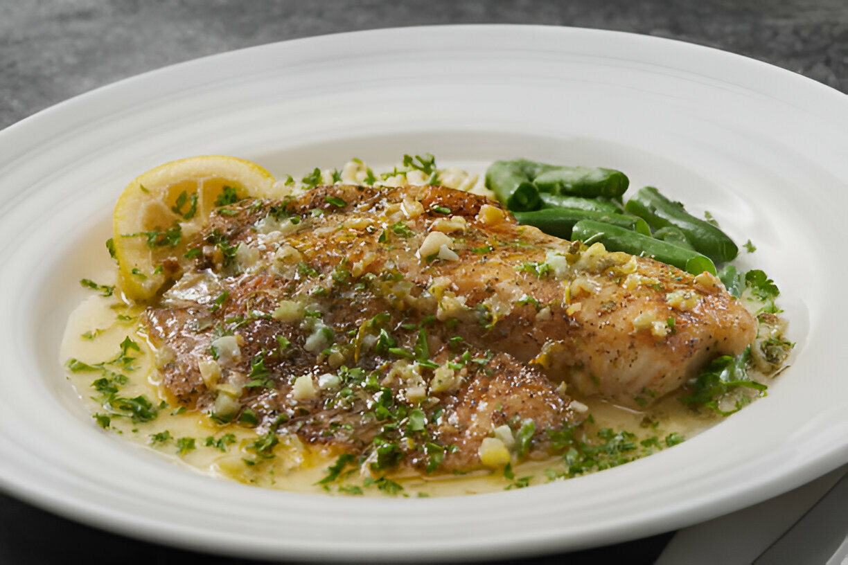 A plate of grilled fish garnished with herbs, served with lemon slices and green beans.