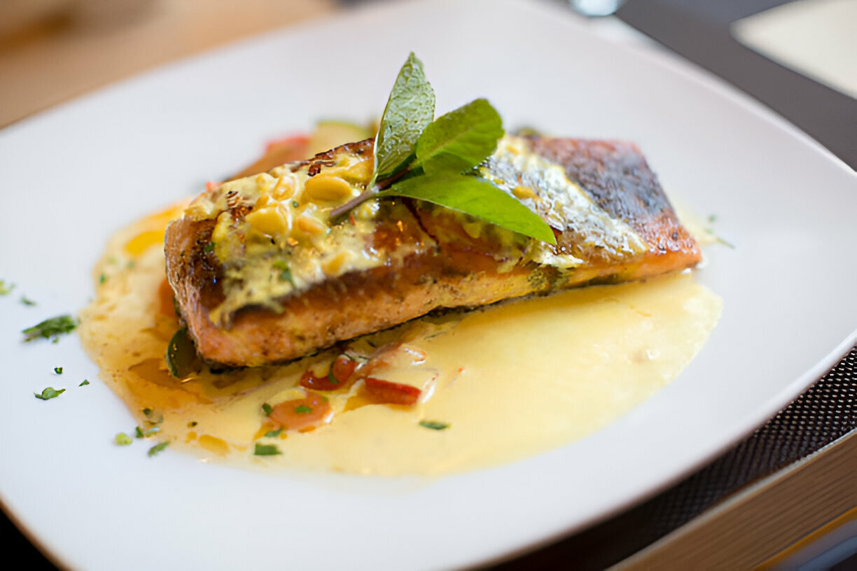 A beautifully plated piece of salmon with a green garnish and sauce on a white plate.