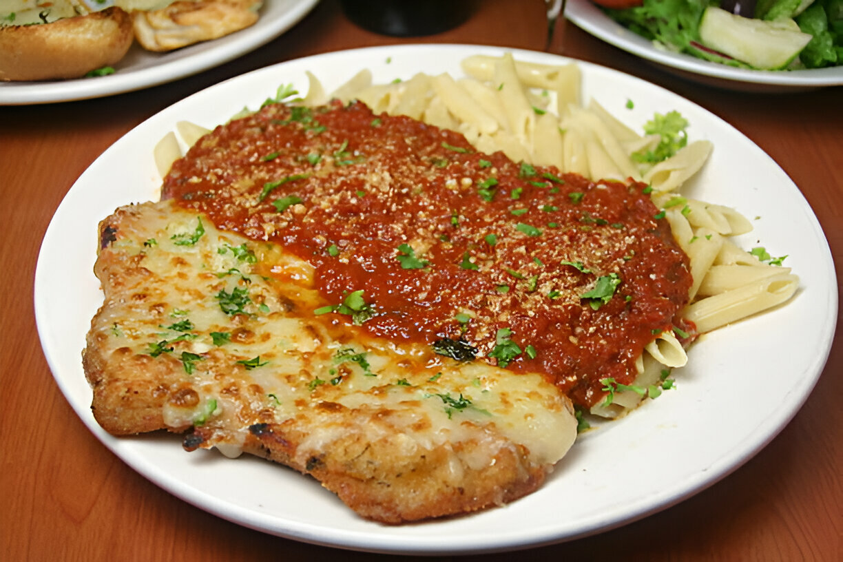 A plate of pasta with marinara sauce and a cheesy chicken dish garnished with parsley.