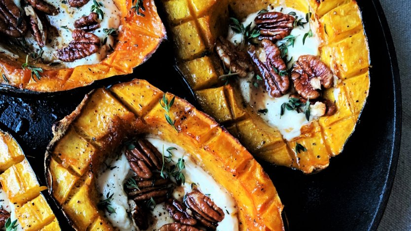 Baked acorn squash halves topped with pecans and herbs served in a cast iron skillet.