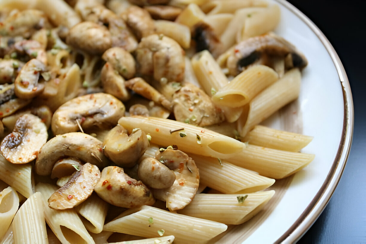 A plate of penne pasta mixed with sautéed mushrooms and spices.