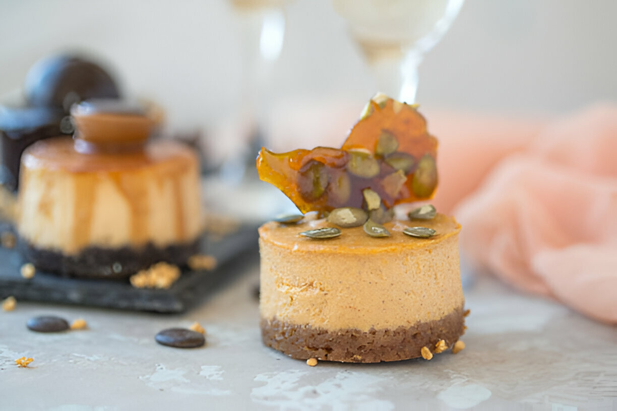 A delicious slice of cheesecake topped with caramel and pumpkin seeds, placed on a marble surface.