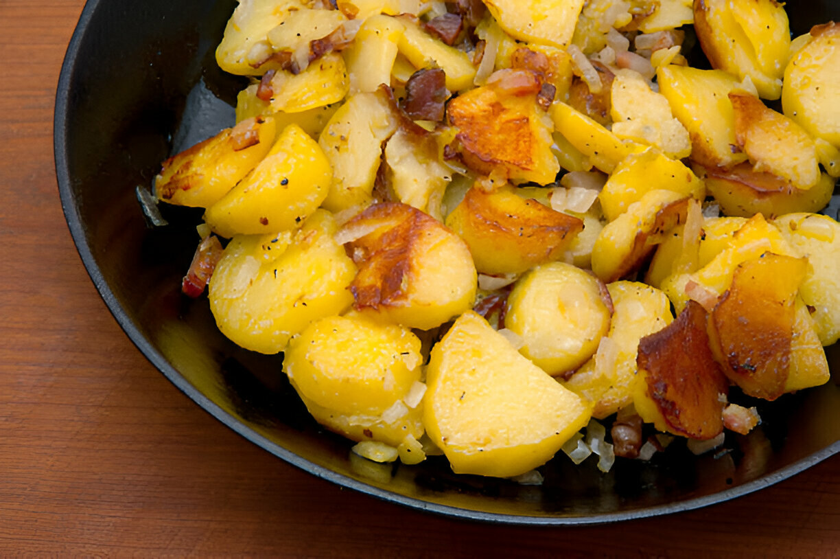 A skillet filled with golden-brown fried potatoes mixed with bits of bacon and onions.