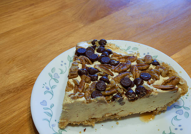 A slice of decadent cheesecake topped with chopped pecans and chocolate chips on a floral plate.