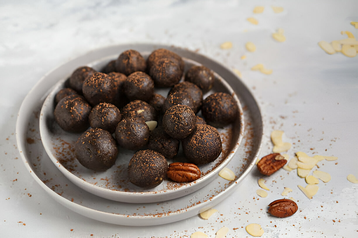 A plate filled with dark chocolate energy balls, surrounded by scattered nuts and almond flakes.