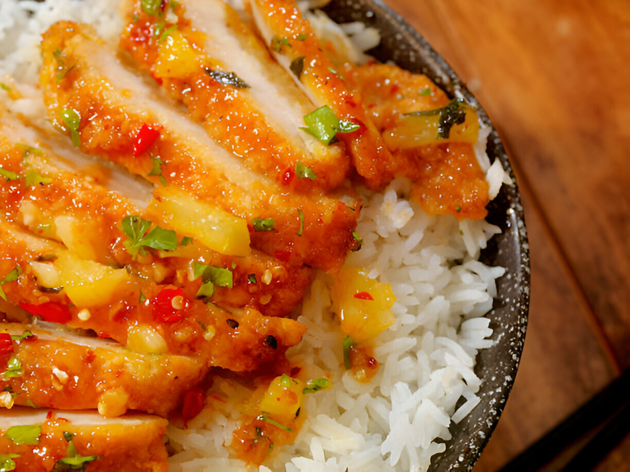 A close-up of sliced chicken with a sweet sauce and pineapple chunks on a bed of white rice.