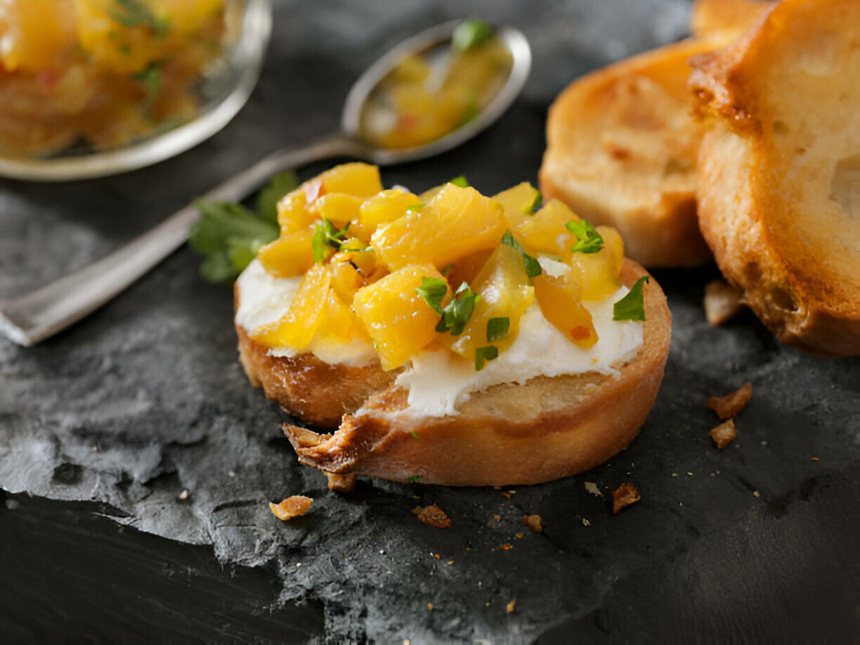 A piece of toasted bread topped with a mixture of diced mango and herbs, placed on a dark slate surface.