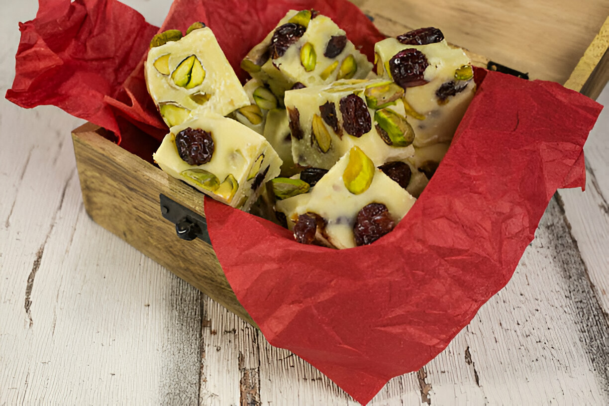 A wooden box filled with pieces of dessert made with pistachios and cranberries, wrapped in red tissue paper.