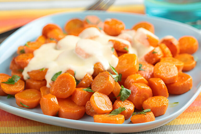 A plate of glazed carrots topped with creamy sauce and garnished with fresh herbs.