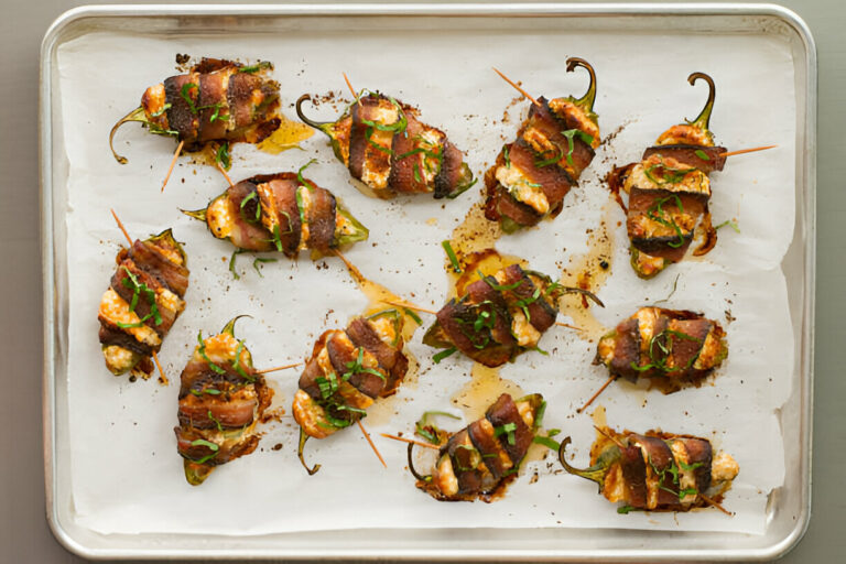 A tray of bacon-wrapped stuffed jalapeño poppers garnished with green herbs on parchment paper.