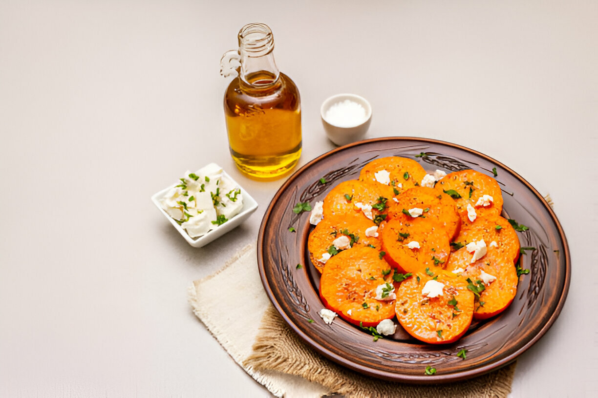 A plate of roasted orange vegetables topped with herbs and cheese, with olive oil and a small bowl of salt on the side.