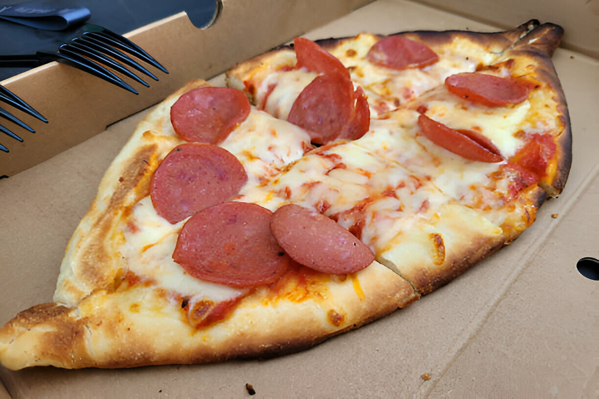 A slice of pepperoni pizza with melted cheese in a cardboard pizza box.