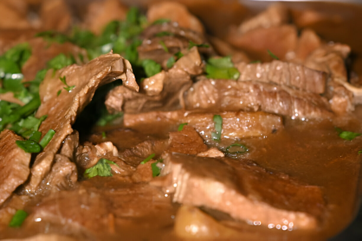 A close-up of beef slices cooked in savory brown sauce, garnished with fresh green cilantro.