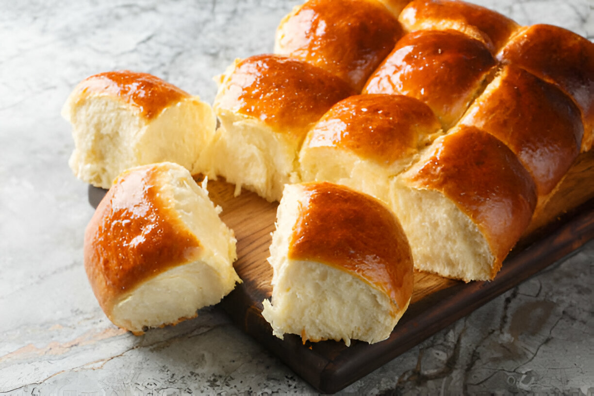 Freshly baked golden brown dinner rolls on a wooden cutting board with a few pieces cut off.