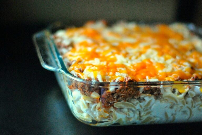 A close-up of a baked casserole dish with layers of egg noodles, ground meat, and melted cheese on top.