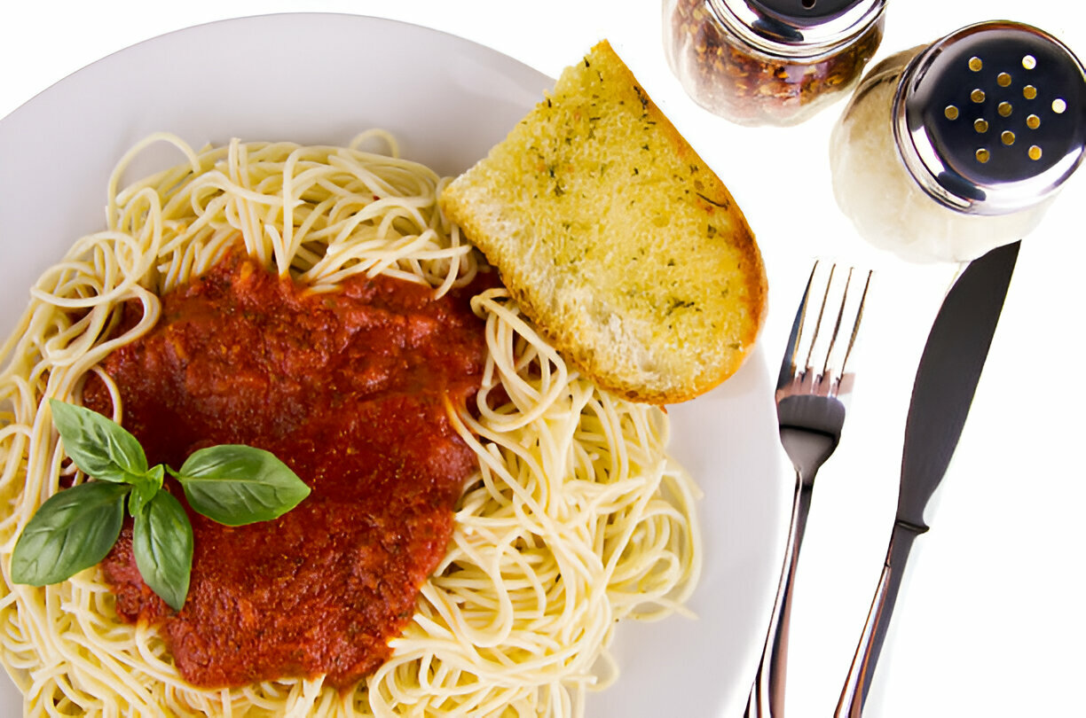 A plate of spaghetti topped with marinara sauce and a slice of garlic bread, accompanied by salt and pepper shakers.