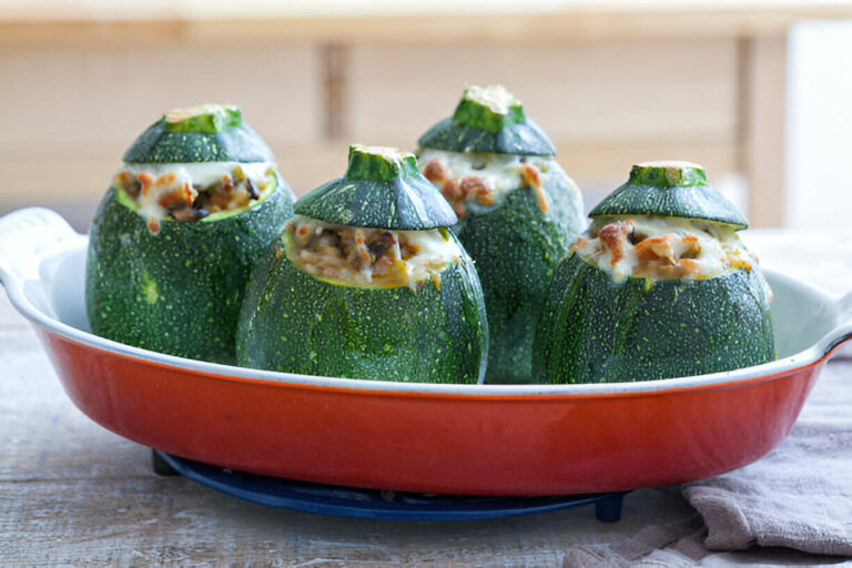 Four zucchini stuffed with a savory filling in a red baking dish