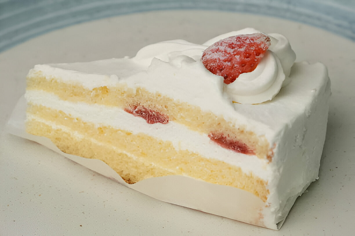 A slice of layered cake with whipped cream and strawberries on top.