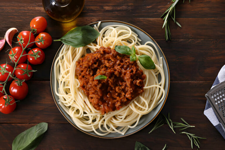 A plate of spaghetti topped with meat sauce and fresh basil, surrounded by cherry tomatoes and herbs.