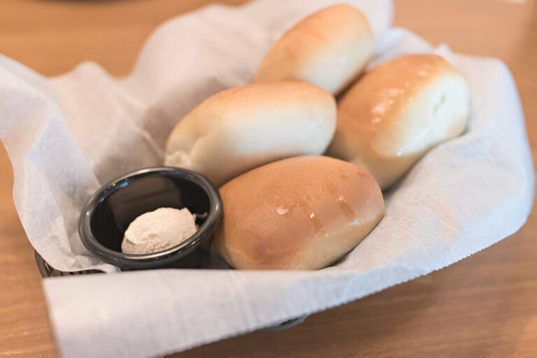 A basket of freshly baked rolls with a small bowl of powdered substance.