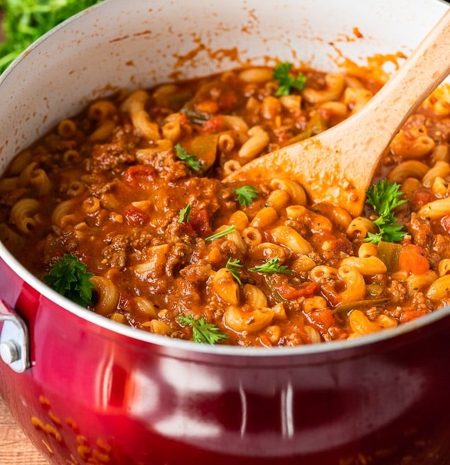 A pot of beef and macaroni pasta cooked in a red saucepan with a wooden spoon