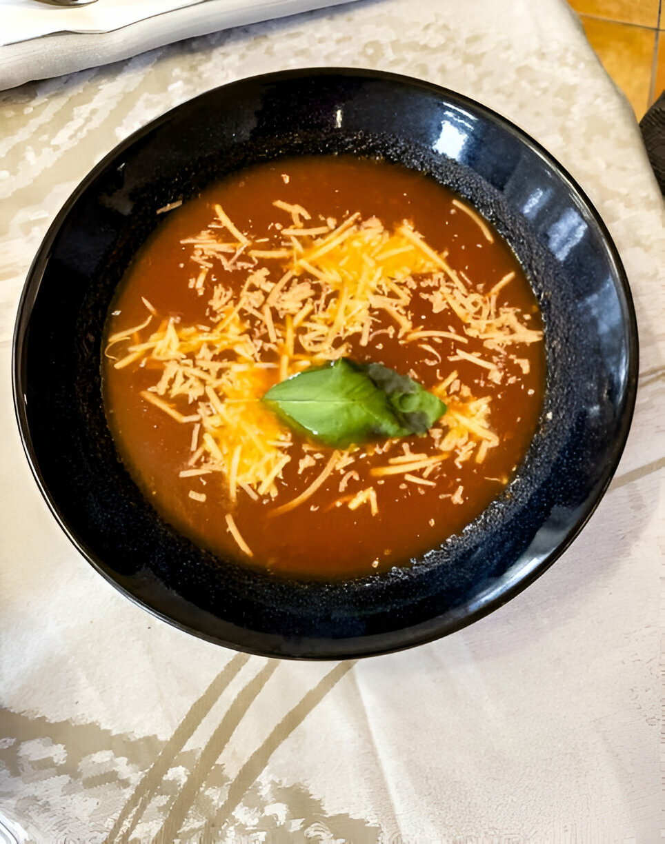 A bowl of soup garnished with shredded cheese and a basil leaf.